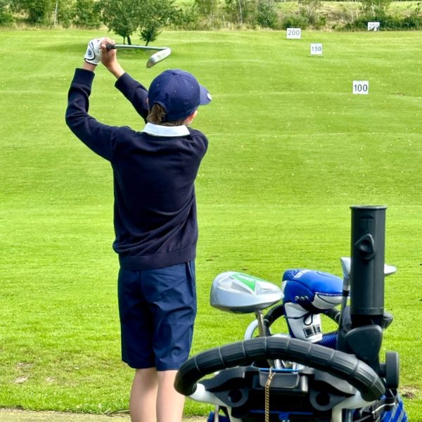 Golfkid beim Abschlag auf der Driving Range mit vollem Golfbag